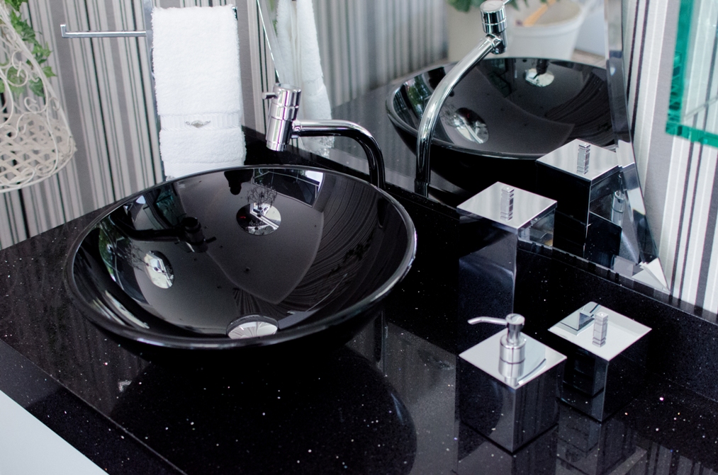 A imagem mostra uma cuba de vidro preta instalada em uma bancada de banheiro, que também é preta.