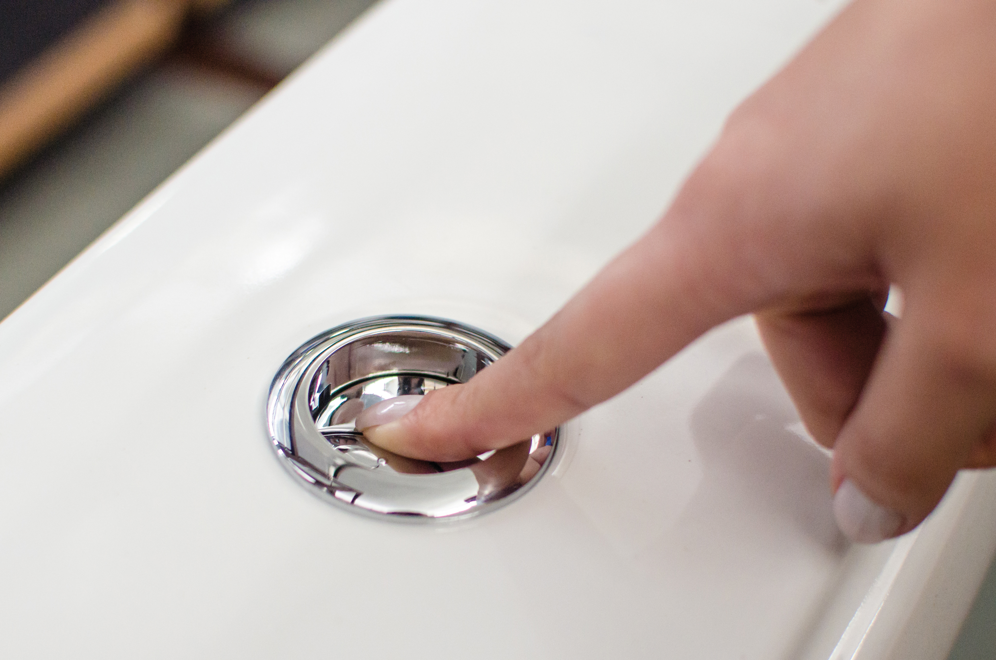 A imagem mostra o dedo de uma pessoa pressionando um botão prateado de descarga acoplada.