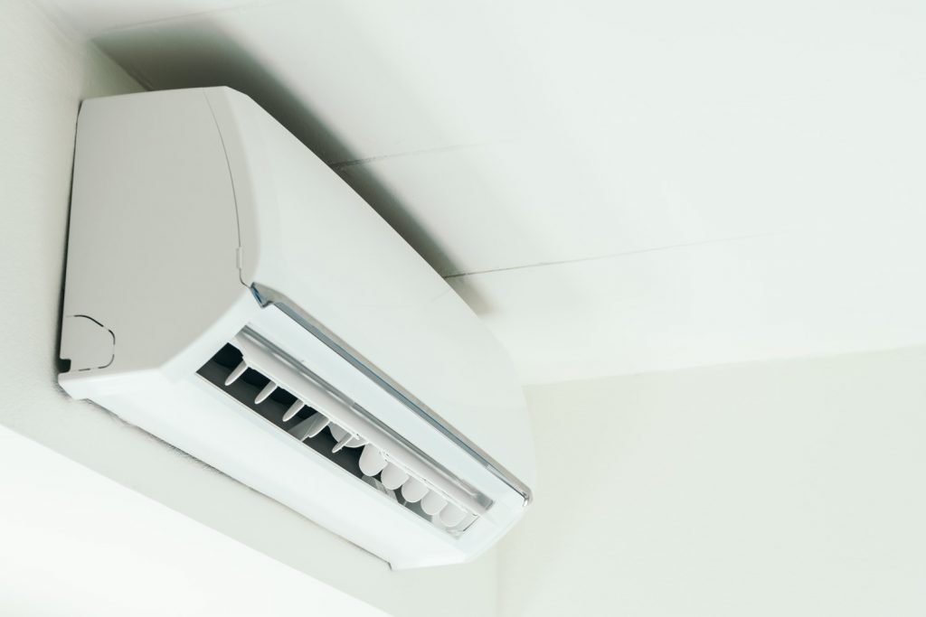 A imagem mostra um ar-condicionado instalado no alto de uma parede, bem próximo ao forro do local.