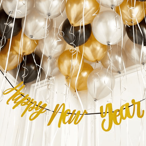 Bexigas prateadas, douradas e pretas com fitas suspensas no teto com um letreiro de “feliz Ano Novo” dourado, escrito em inglês.