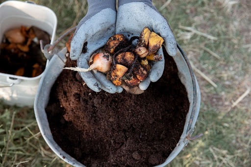 Mãos com luvas seguram material orgânico acima de um balde com terra.