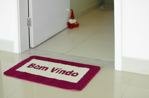 Entrada de uma casa com tapete escrito “bem-vindo” em vermelho e branco, e um encosto de porta em formato de papai noel.