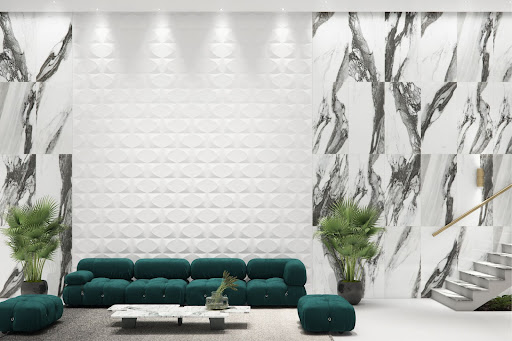 Sala de estar ampla, com porcelanato branco com veios, que lembram mármore, e uma parte com revestimentos 3D. A iluminação de destaque está acima, com o uso de spots. Um grande sofá verde, com poltronas de apoio na mesma cor em cada extremidade. Entre o sofá e as poltronas, há dois vasos com plantas. 