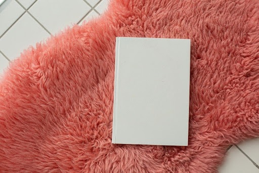 Um dos tipos de tapetes, o shaggy rosa aparece sobre um piso branco, com uma folha de papel em cima.