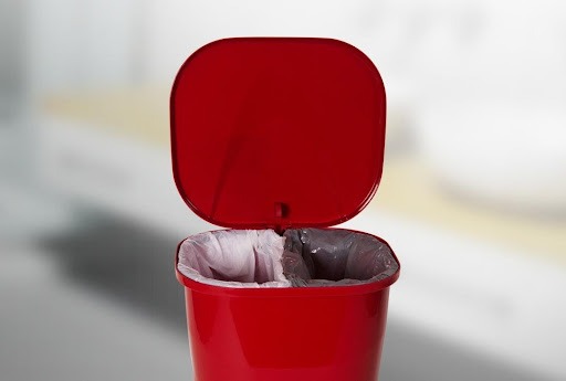 Uma lixeira ecológica da Astra na cor vermelha. Ela está aberta e é possível ver seu interior, com os dois sacos de lixo.