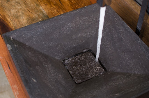 Uma torneira preta aberta, com água caindo em uma cuba também preta, instalada sobre um gabinete de madeira.