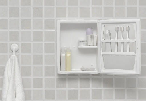 Um armário de banheiro aberto, com alguns produtos dentro, incluindo um tubo de pasta de dente e três escovas. Ao lado, um porta-toalhas, com uma toalha pendurada.