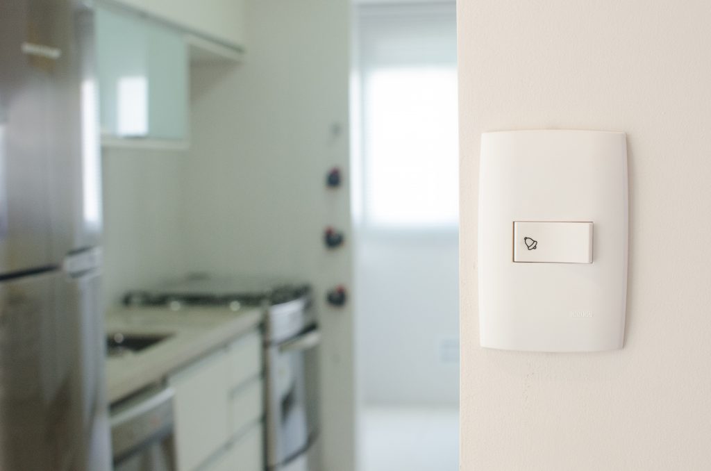 Interruptor branco da Astra instalado na parede de uma casa, especificamente na cozinha. Ao fundo, fora de foco, é possível ver os eletrodomésticos, como geladeira e fogão, a pia e alguns armários.