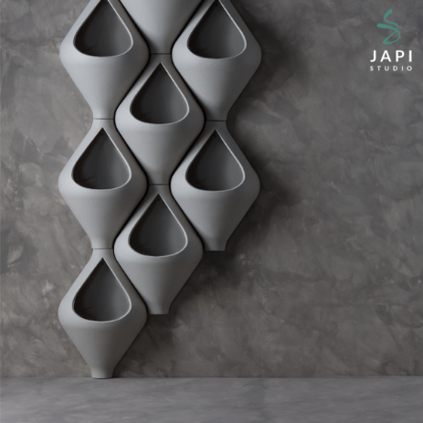 Uma parede de cimento queimado apresenta vários vasos de gota da linha Japi Studio, fazendo uma composição.
