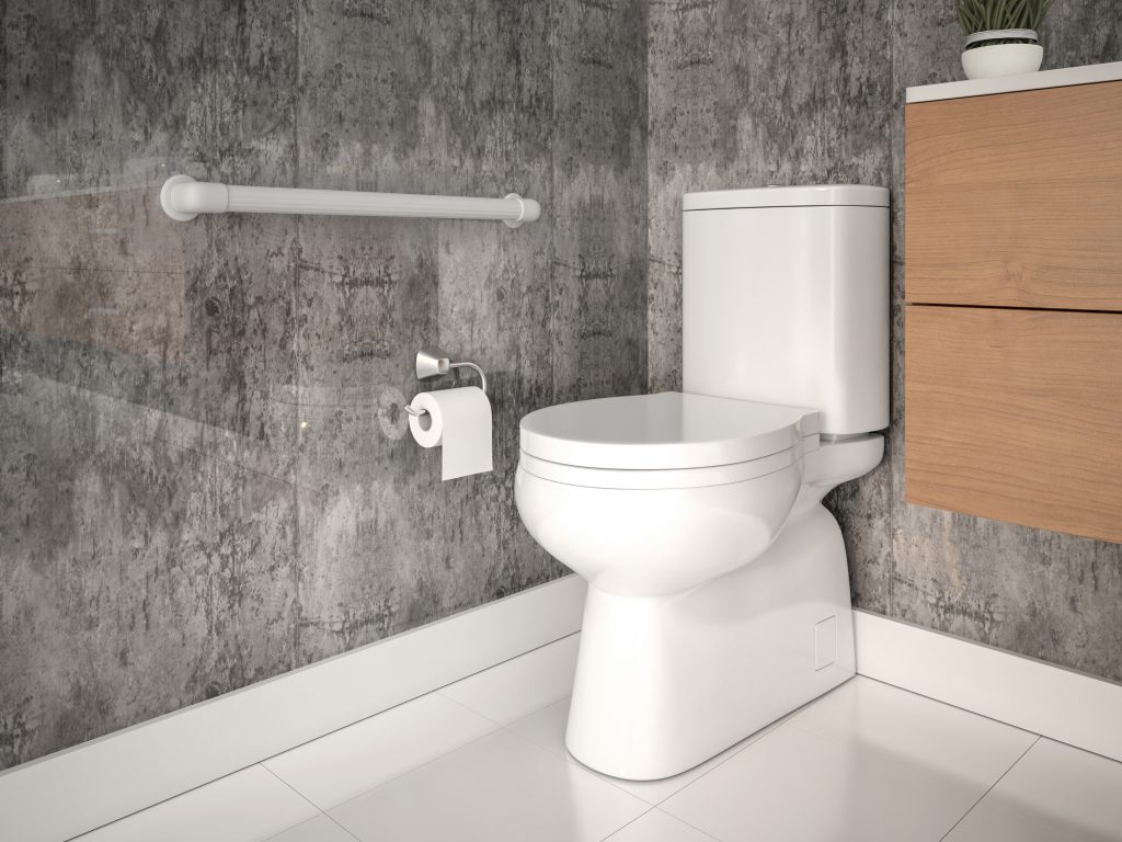Em um banheiro com paredes em cimento queimado, há um vaso sanitário com caixa acoplada na cor branca. Ao lado esquerdo está  uma barra de apoio reta branca, fixada na parede. O ambiente é composto por um porta-papel higiênico e um gabinete de madeira ao lado direito.