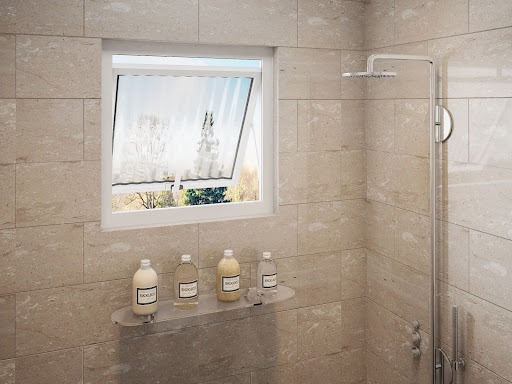 A imagem apresenta um box de banheiro com um chuveiro prata na direita, uma estante com produtos de banheiro e uma esquadria pequena branca.
