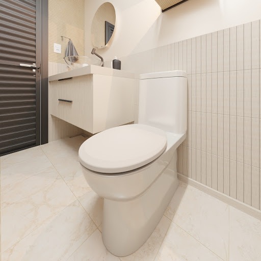A imagem acima apresenta um banheiro com tons de bege, um vaso e assento sanitário branco,  uma bancada com gavetas, cuba transparente, espelho redondo e uma porta preta na lateral esquerda. 