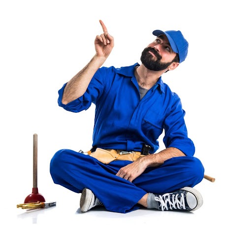 Um encanador experiente, vestindo um macacão azul, está agachado no chão com as pernas cruzadas. Ele aponta com o dedo indicador para o lado esquerdo, enquanto olha para cima com uma expressão confiante. Ao lado dele, estão um desentupidor e um alicate, ferramentas essenciais para o seu trabalho.